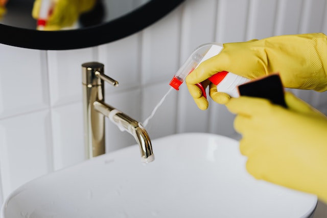 person wearing yellow cleaning gloves to scrub a bathroom sink